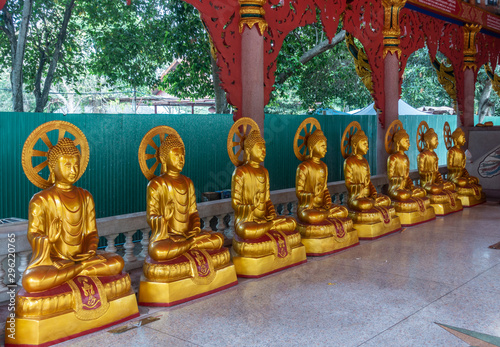 Bang Saen, Thailand - March 16, 2019: Wang Saensuk Buddhist Monastery. Line of Golden statues of Bodhisattva on side of main open Prayer Hall. Green foliage outside. photo