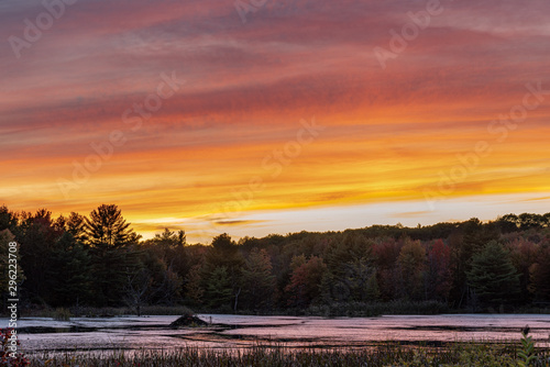 sunset on pond with beaver hut in the distance orange red yellow cloud streaks