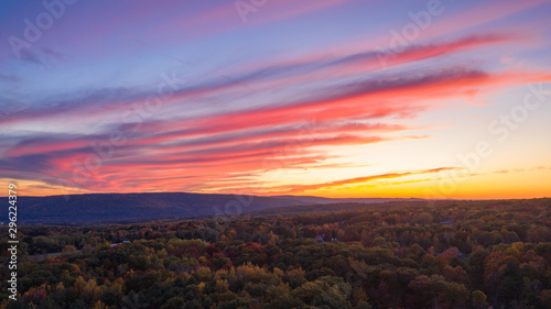 Autumn sunset aerial perspective.   a red blue yellow cloud streaked sky with hills in the background and colored tree tops in the for ground.