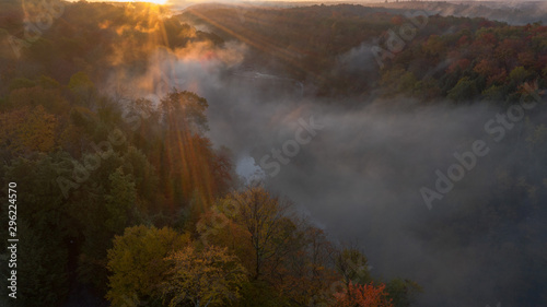 aerial perspective sunrise over a falls on river.  fog is seen over the river and the tree are in full bloom with autumn colors