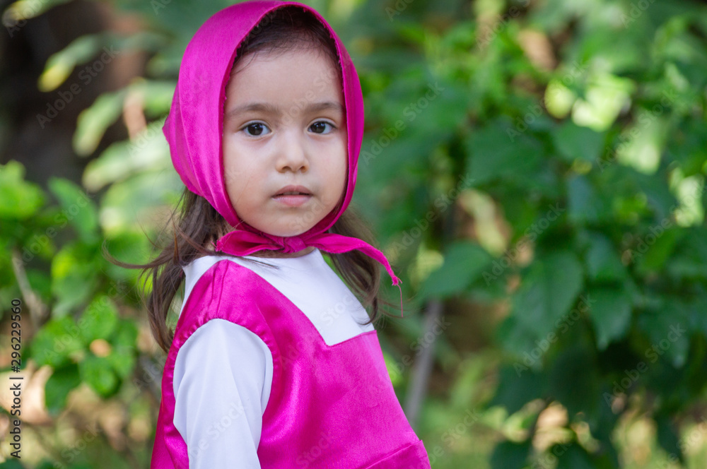 Pretty little girl in pink dress with headscarf plays and walks through the garden flat green grass and trees Pretty little girl in pink dress with headscarf plays and walks through the garden flat green grass and trees