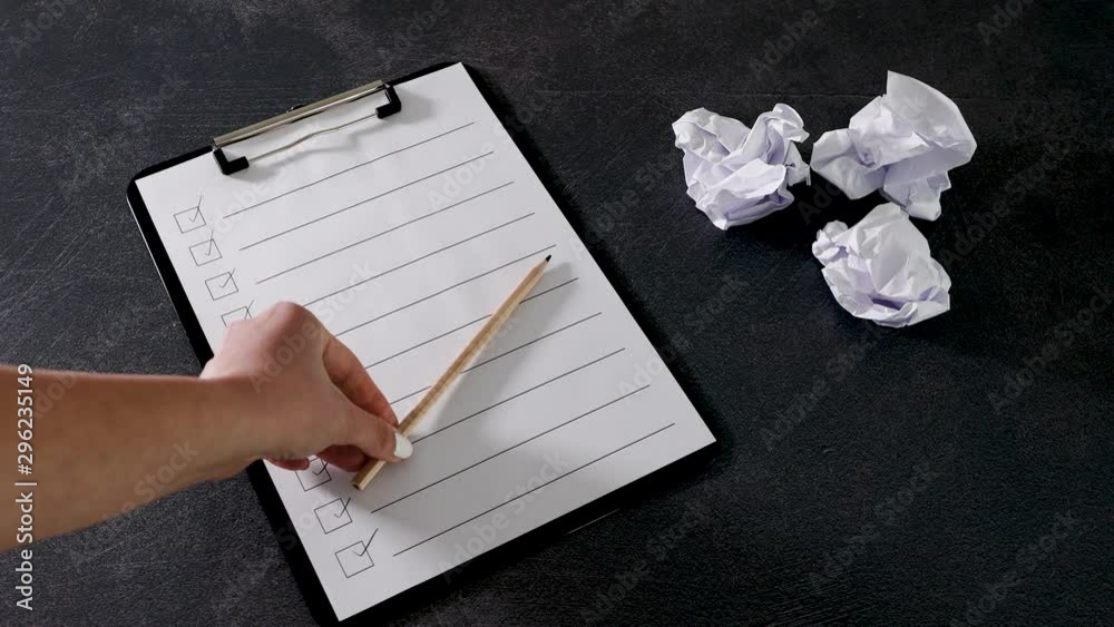lack of productivity concept hand placing pencils in X position on to do list next to group of scrunched paper balls