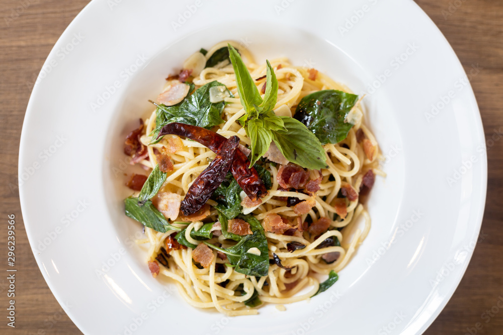 Top view of Stir-Fried Spaghetti With Dried Chili And Crispy Bacon in a White Plate on a wooden table.