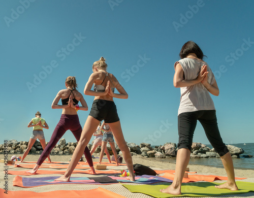 Group of young people has a meditation on yoga class by the sea on a sunny day.