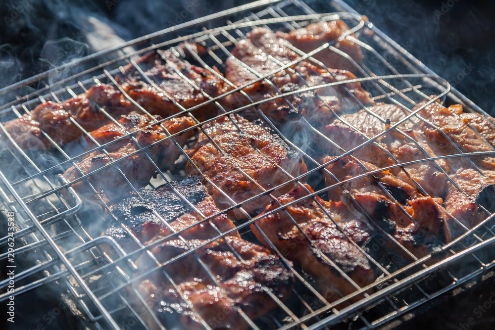 Close-up on the process of cooking shashlik of pork or beef meat clamped in a grill with a crispy burnt crust over gray burnt coals on an open fire with smoke going up.