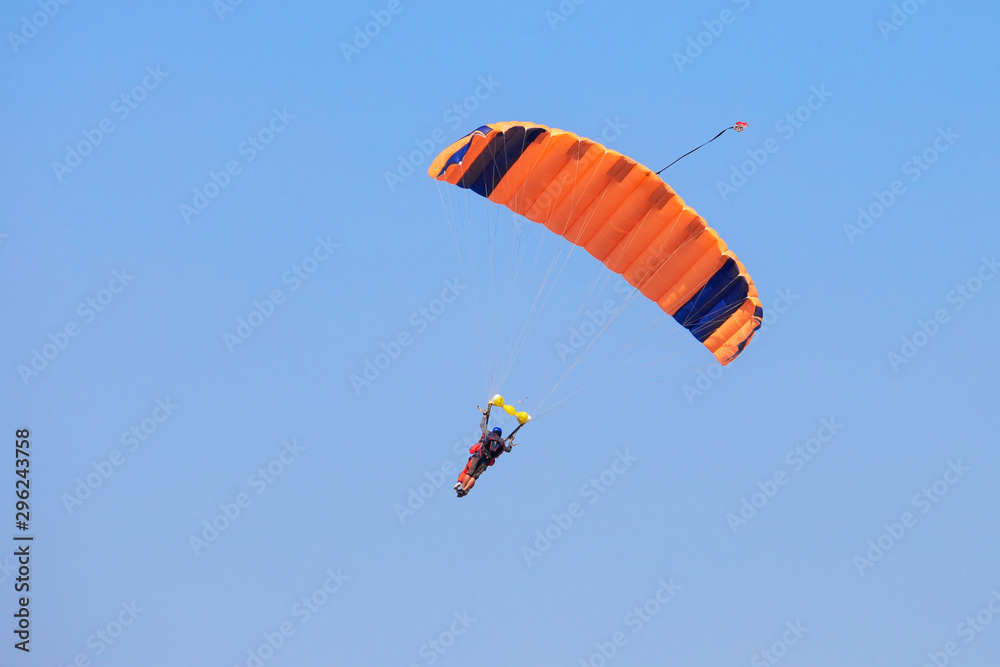 Skydiver under an orange parachute in blue sky Skydiver under an orange parachute in blue sky