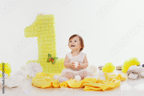 Birthday celebration: girl sitting on the floor among the decoration: numbers 1, artificial flowers and white balls photo