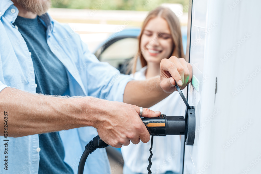 Man holding power cable supply plugged in public charging station Man holding power cable supply plugged in public charging station