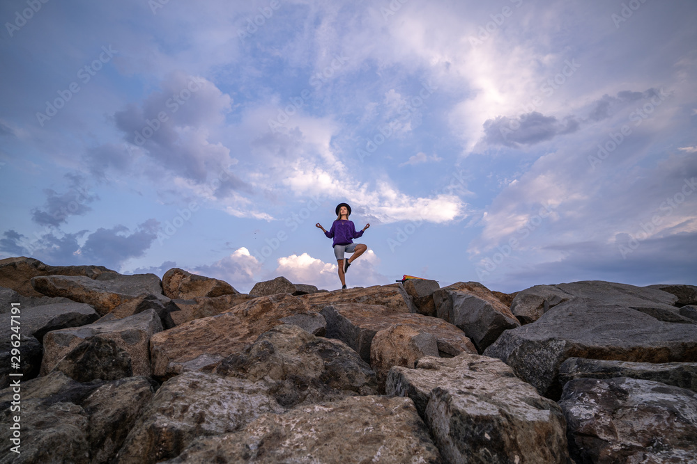 Lonely woman in hat meditates on stones against a cloudy blue sky, enjoying freedom, tranquility and pacification. Zen search