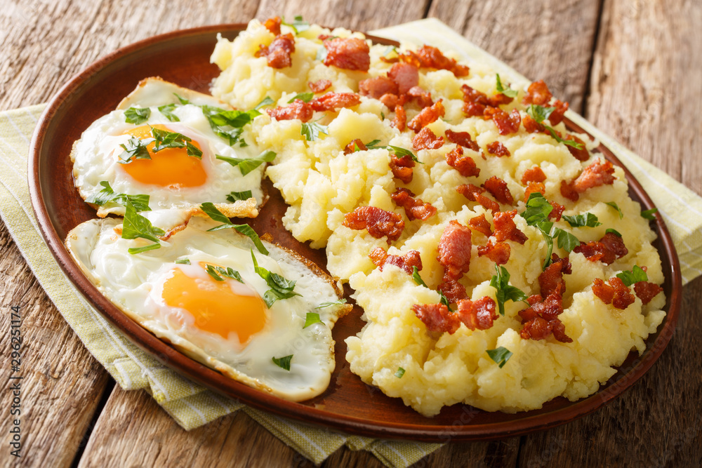 Tasty hot mashed potato with bacon and parsley served with fried eggs close-up on a plate. horizontal Tasty hot mashed potato with bacon and parsley served with fried eggs close-up on a plate. horizontal