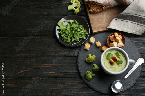 Flat lay composition with cup of broccoli cream soup on black wooden table, space for text