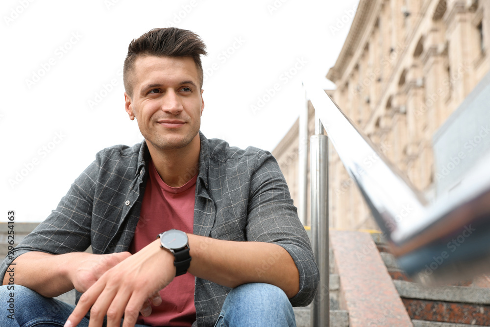 Fototapeta premium Portrait of handsome young man sitting on stairs outdoors