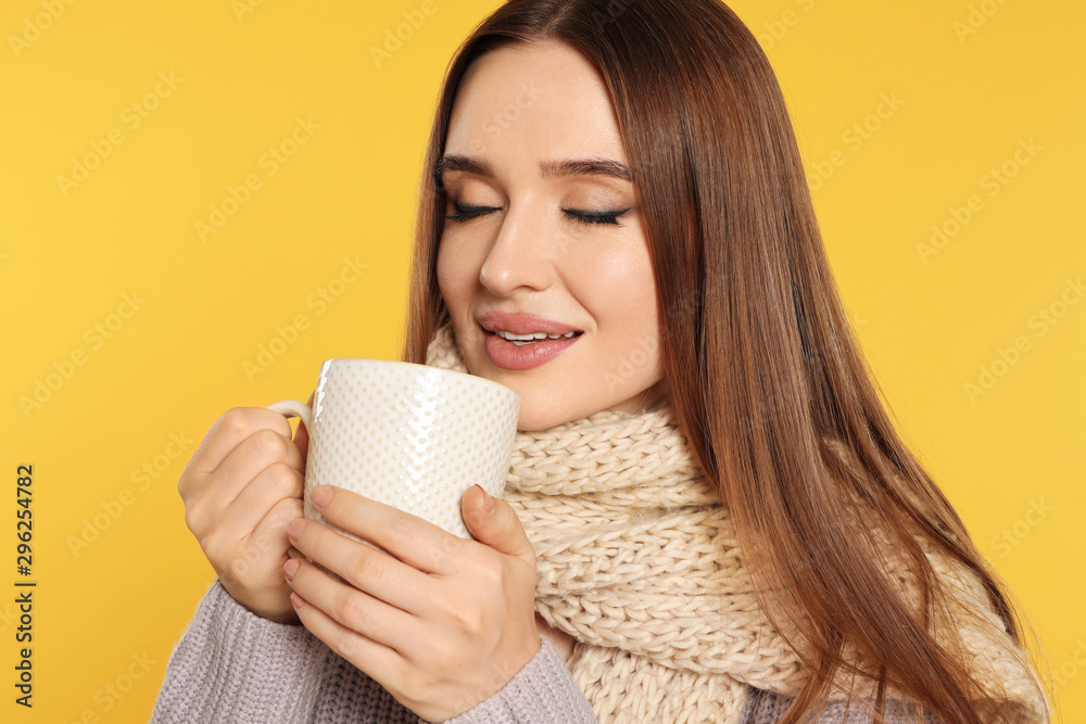 Beautiful young woman in sweater with drink on yellow background. Winter season Beautiful young woman in sweater with drink on yellow background. Winter season