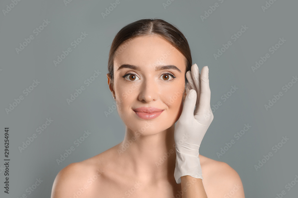 Doctor examining woman's face before plastic surgery on grey background Doctor examining woman's face before plastic surgery on grey background