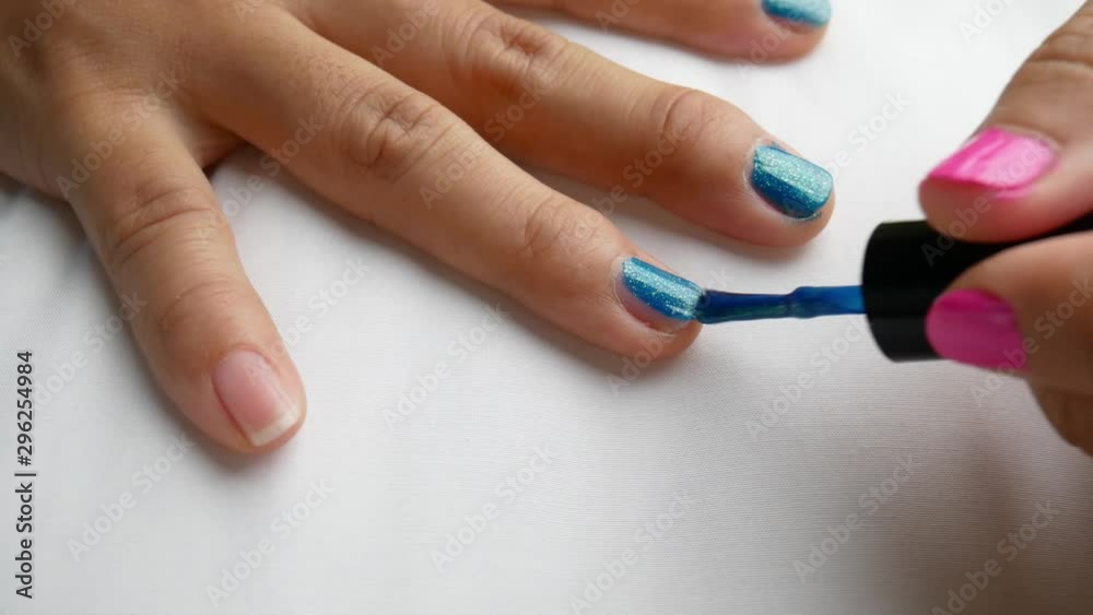 Close-up of female hands painting blue nail varnish, self made manicure at home. Close-up of female hands painting blue nail varnish, self made manicure at home.