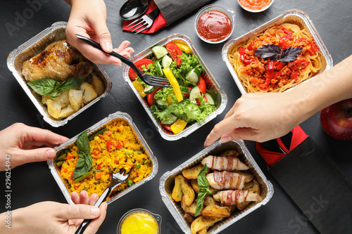 People eating from lunchboxes at grey table, top view. Healthy food delivery photo