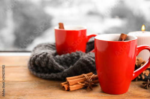 Cups of hot winter drink with scarf on window sill indoors