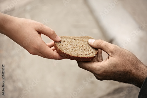 Fototapeta Woman giving poor homeless person pieces of bread outdoors, closeup