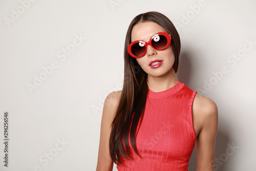 Beautiful woman in stylish sunglasses on light background, space for text