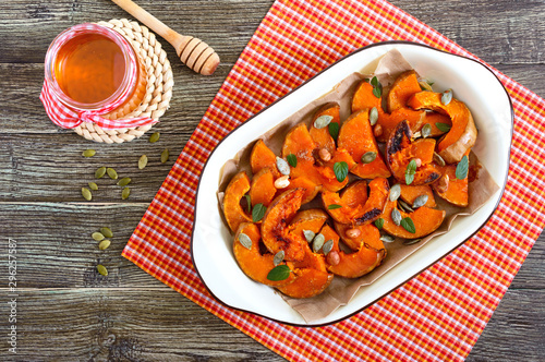 Pumpkin slices baked in the oven with honey, nuts, cinnamon, seeds, mint. Pieces of pumpkin lying on the baking paper in a bowl. Healthy food, dessert for gourmets. Traditional autumn snack in Hungary