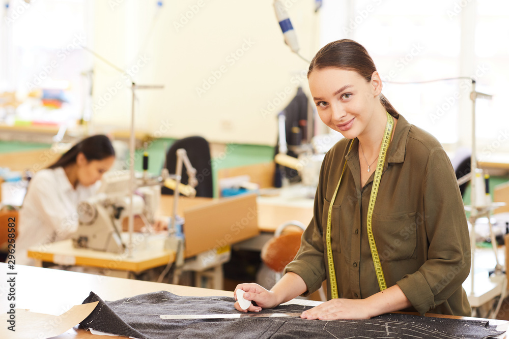 Portrait of young tailor looking at camera while making pattern on fabric for future dress in workshop Portrait of young tailor looking at camera while making pattern on fabric for future dress in workshop