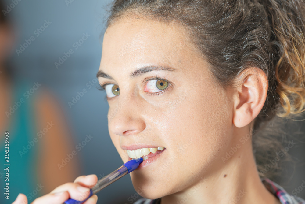 Beautiful and charming woman with big green eyes and brown hair, biting a pencil with her white teeth, with the background out of focus. Beautiful and charming woman with big green eyes and brown hair, biting a pencil with her white teeth, with the background out of focus.