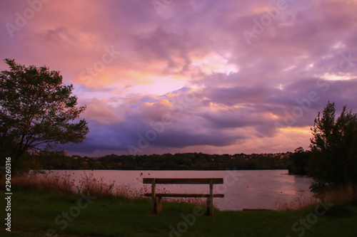 Romantic sunset over the water. Bench in foreground. Rural scene with dramatic sky.  photo