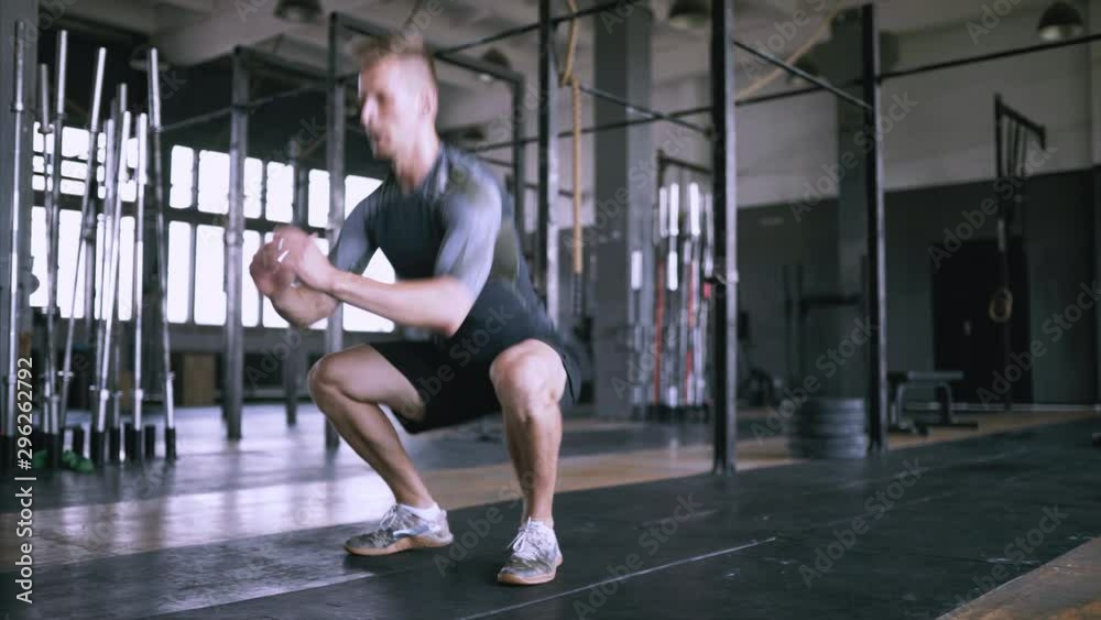 Jumping squats at gym. Male fitness instructor showing squat exercise