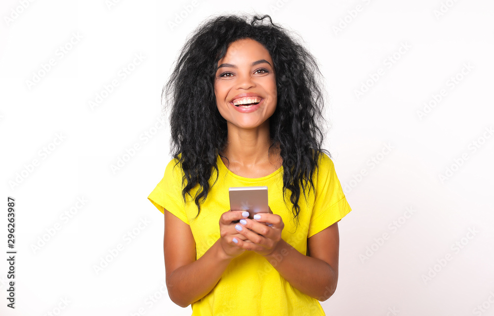 Always online. Front portrait of a joyful African American girl with shoulder-length messy black hair, who is laughing sincerely while holding a smartphone in her hands. Always online. Front portrait of a joyful African American girl with shoulder-length messy black hair, who is laughing sincerely while holding a smartphone in her hands.