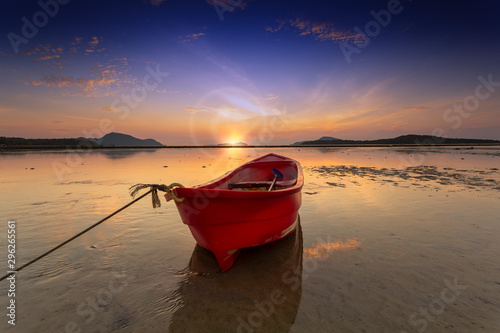 Sunrise morning time alone red fishing boat on the beach and low tide sea background.