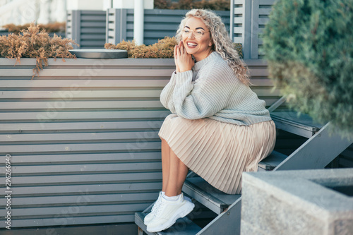 Plus size model with blond curly hair in knitted sweater outdoor photo