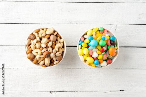 Diet decision concept. Mixed nuts and sweet in bowls on white wooden background. Top view