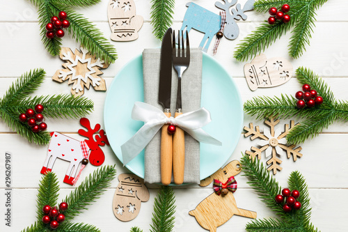 Top view of New Year dinner on festive wooden background. Composition of plate, fork, knife, fir tree and decorations. Merry Christmas concept