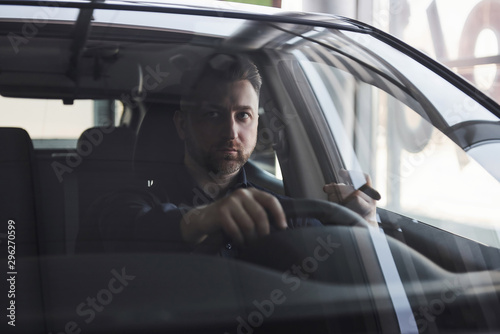 Having busy day. Front view of young bearded businessman sitting in his luxury black car