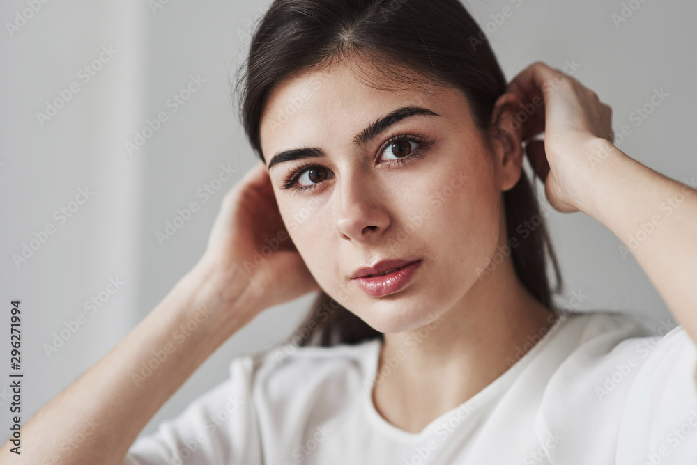 Touching the hair. Young brunette in the room with white walls and daylight that comes from the window Touching the hair. Young brunette in the room with white walls and daylight that comes from the window