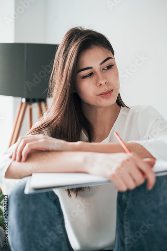 Grey lamp at background. Young brunette in the room with white walls and daylight that comes from the window