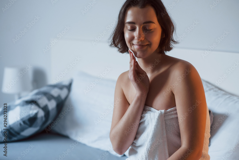 Time for a make up. Woman sits on the bed and use cosmetics to clean her skin Time for a make up. Woman sits on the bed and use cosmetics to clean her skin