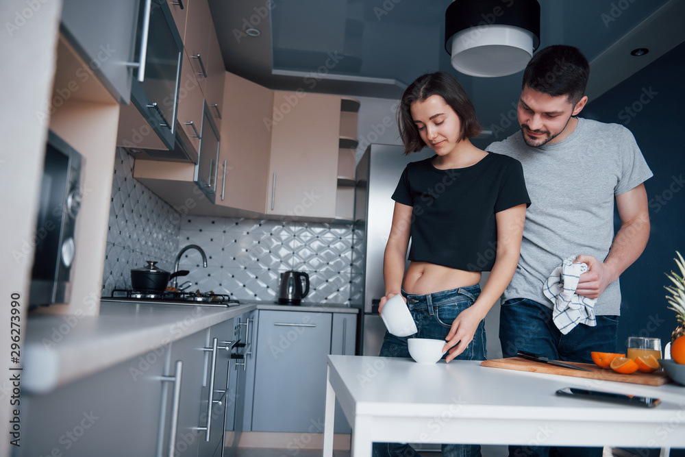 Obraz premium Pouring the water. Young couple in the modern kitchen at home at their weekend in the morning time