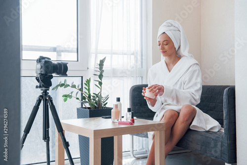 Towel on the head. In front of camera on the tripod. Conception of fashion and skincare. Brunette girl uses cosmetics