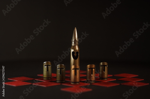 A hand-crafted chess pieces made of bullet shells (7.62x54 mm and 7.62x39 mm caliber). Chess game. Pawns guard the king. Dark background. The small depth of field