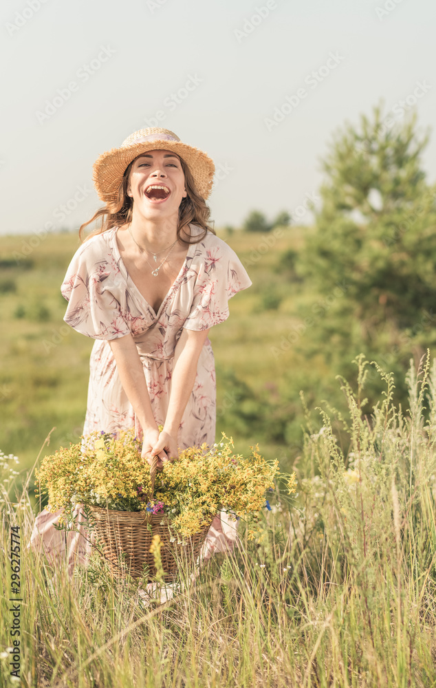 Obraz premium girl with a basket of flowers and a straw hat in a summer field