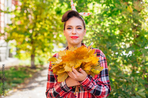 Beautiful woman with make up and hair in pin up holding big bouquet of maple yellow leaves.