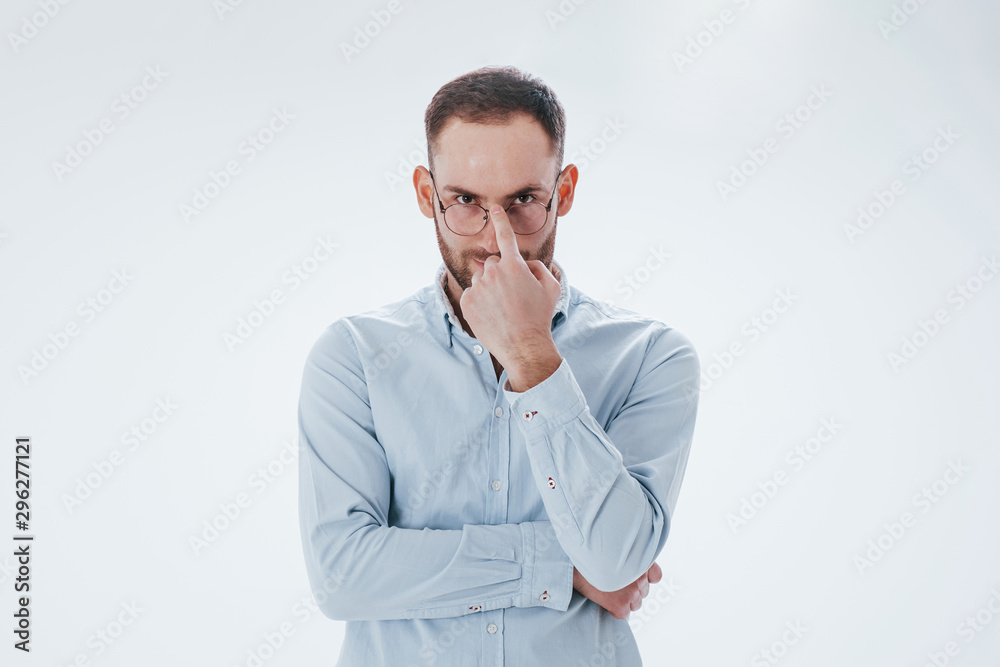 Putting glasses on. Man in official clothes stands against white background in the studio Putting glasses on. Man in official clothes stands against white background in the studio
