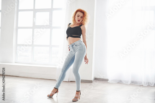 Full height photo. Attractive redhead woman posing in the spacey room near the window