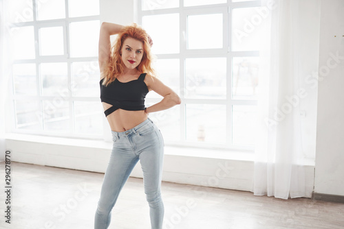 Front view. Attractive redhead woman posing in the spacey room near the window
