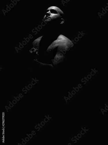 Low key black and white photo of a hairy chested man flexing his left arm while looking towards the light