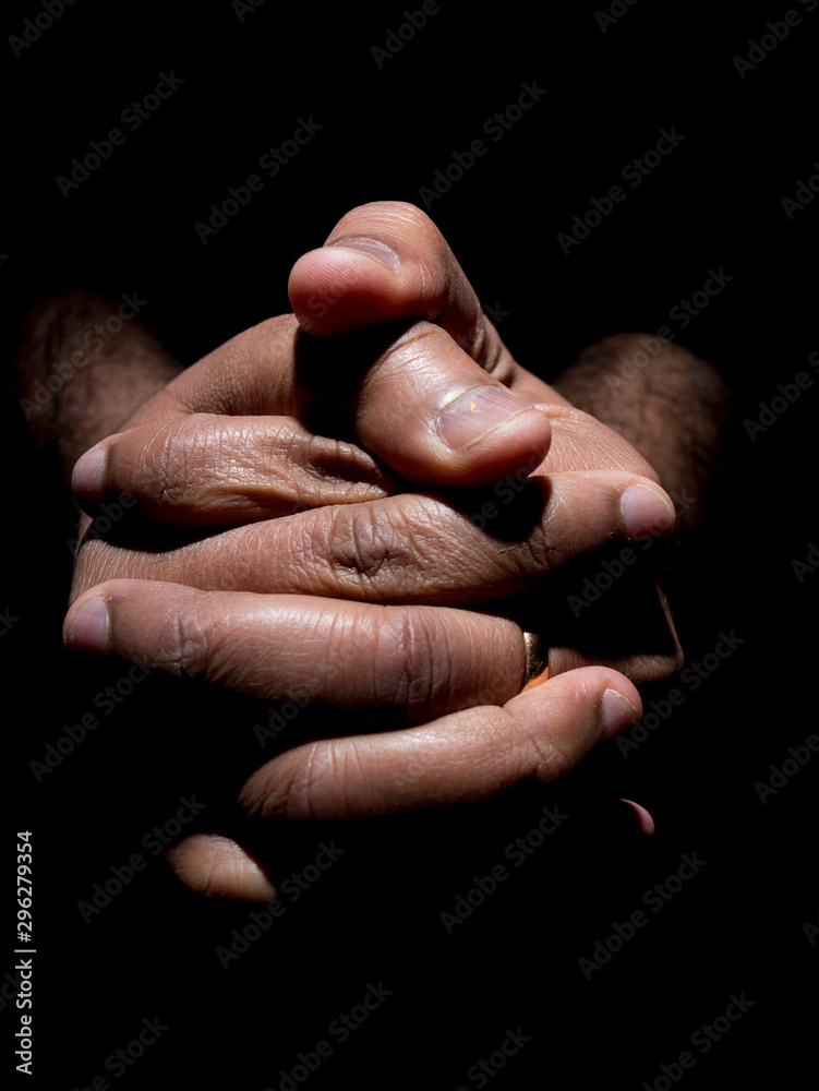 Close up of a brown mans clasped hands in low key lighting