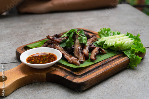 Sun dried Thai fried Beef Jerky meal Nua Dad Deaw served on wooden chopping board with spicy chilli dipping sauce - Authentic North Eastern Thailand meal in a trendy Asian outdoors restaurant concept