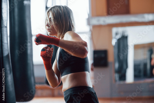 Aggressive kick. Female boxer is punching the bag. Blonde have exercise in the gym © standret