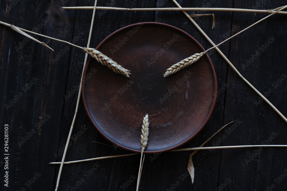 three wheat spikelets on a clay plate on a black burnt